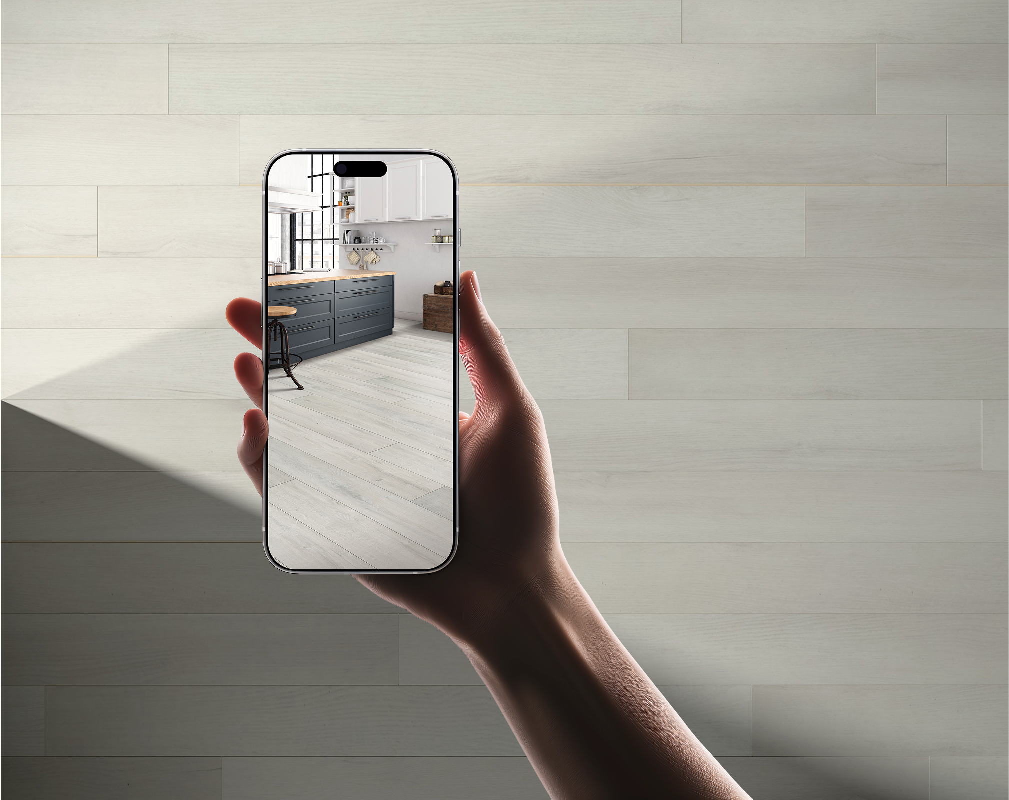 A hand holds a smartphone, which displays a modern kitchen with white cabinets and a dark blue island. The phone’s screen blends seamlessly with the TORLYS flooring in light wood tones featured in the background.