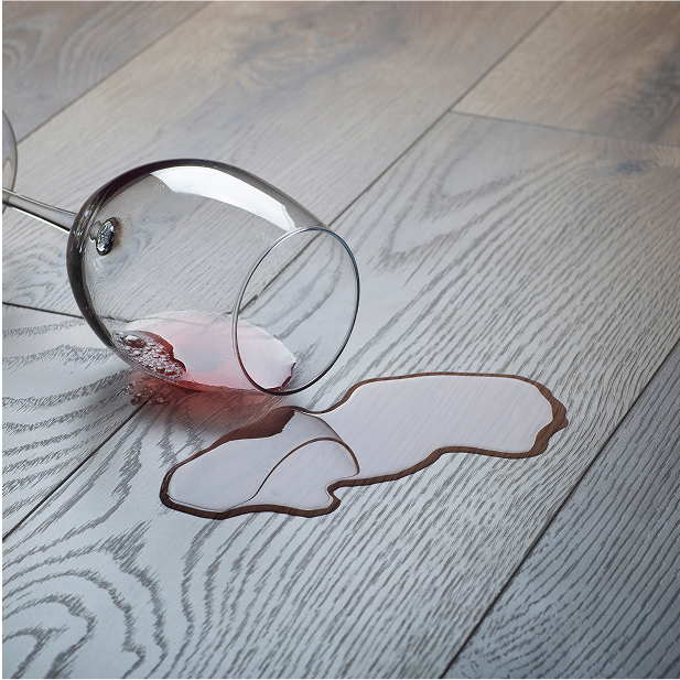 A wine glass tipped over on a wooden floor, with red wine spilled across the light-colored smart floors.