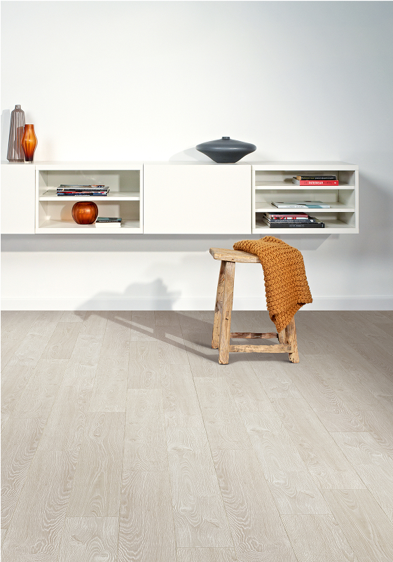 Minimalist room with smart floors in light wood, white floating shelves displaying decor, and a rustic wooden stool draped with a brown knit blanket. A crisp white wall provides a clean background.