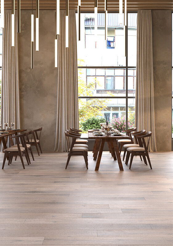 Modern dining area with wooden tables and chairs, TORLYS flooring, large windows with sheer curtains, and hanging linear pendant lights. Trees and a building are visible outside through the windows.